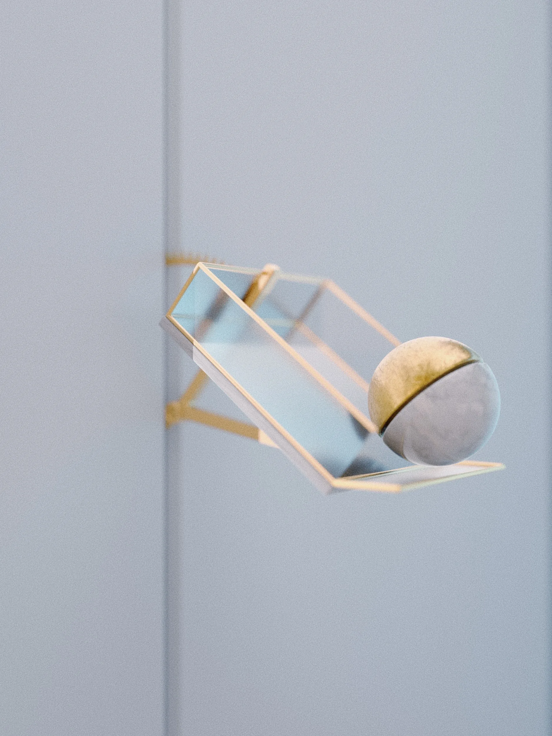 Golden geometric frame holding a beige sphere against a pale background.